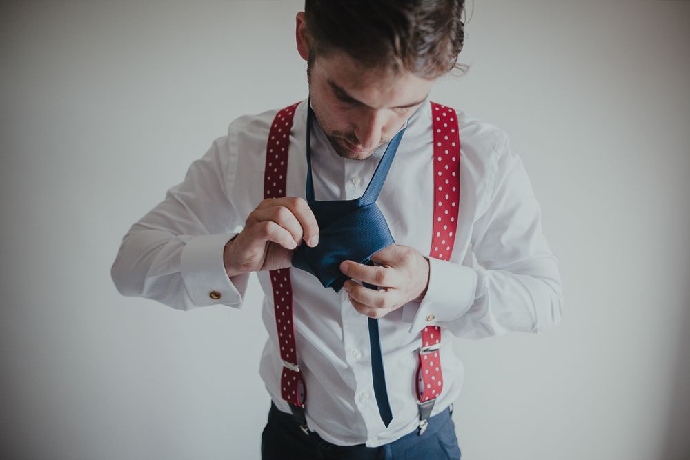 Person in white shirt and red polka dot suspenders adjusting blue tie.