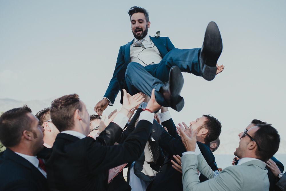 Celebratory moment as groomsmen toss someone into the air during wedding festivities.