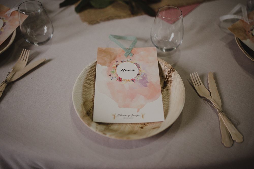Pink floral wedding menu card placed elegantly on white plate with silverware at formal table setting.