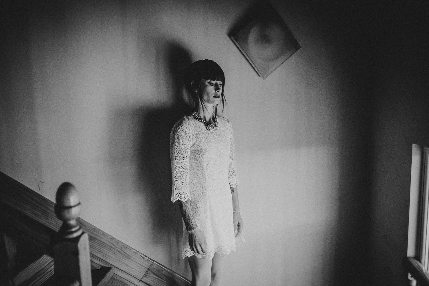 Moody black and white portrait of person standing near staircase with dramatic lighting.