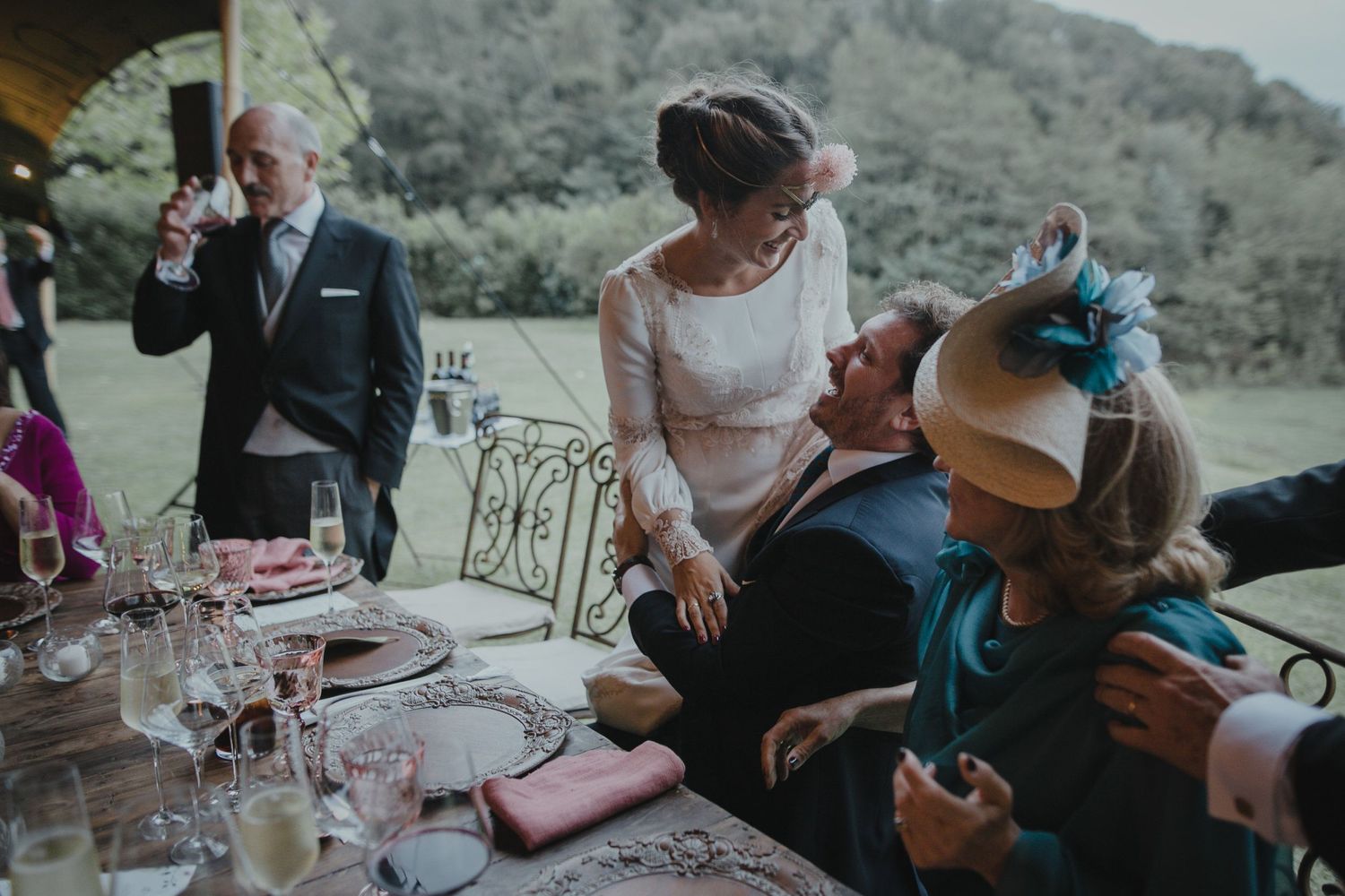 Wedding guests sharing a joyful moment around a decorated table at an outdoor reception.