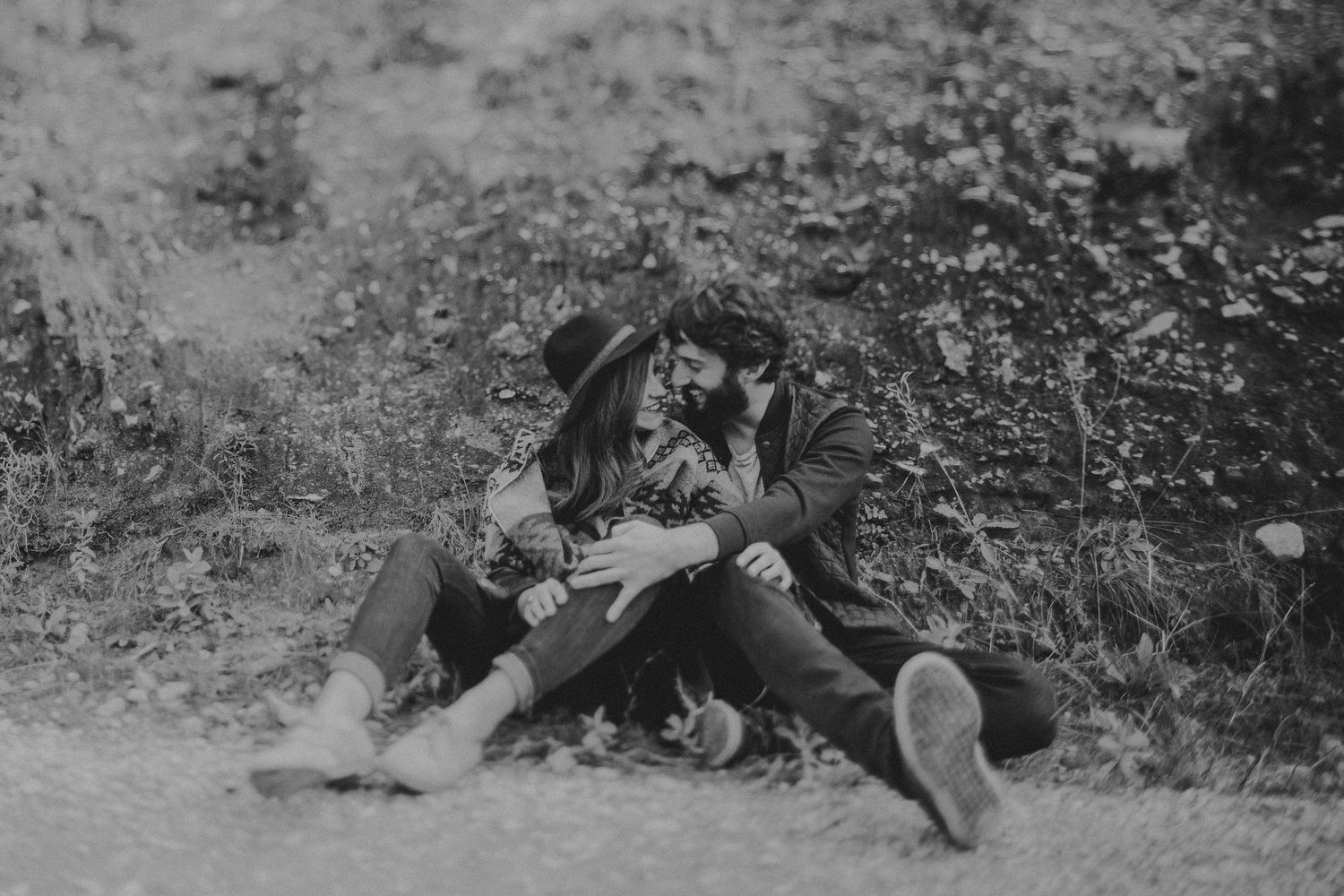 A black and white image of a couple relaxing together on the ground outdoors.