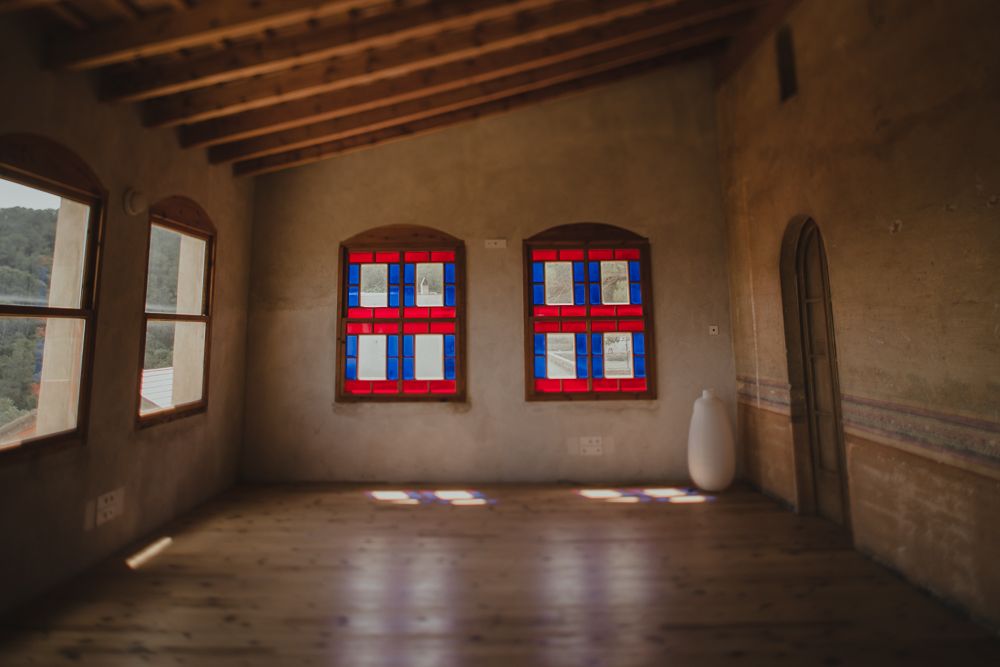 Empty room with wooden floors and two colorful striped windows in an adobe-style building.