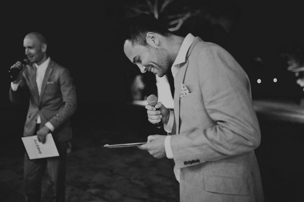 Two people in formal attire share a joyful moment reading papers at an outdoor nighttime event.