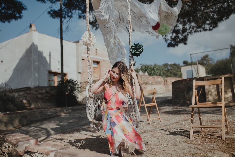 Person in floral dress sitting on swing with white ghost decorations in outdoor setting.