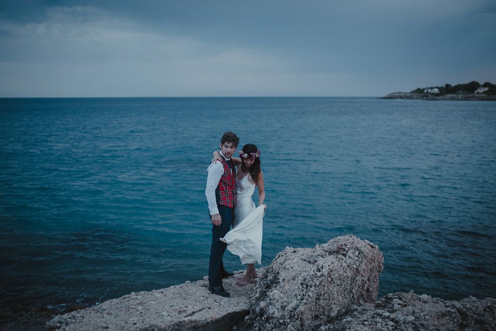 Intimate coastal wedding portrait with blue ocean backdrop and rocky foreground.