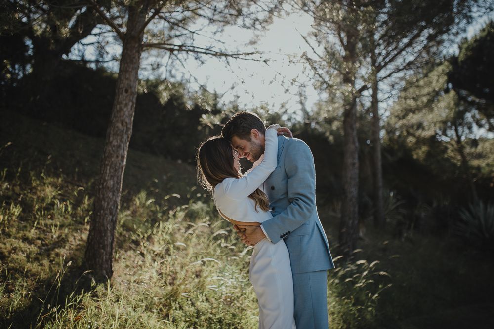 Intimate moment between newlyweds embracing among pine trees in natural lighting.