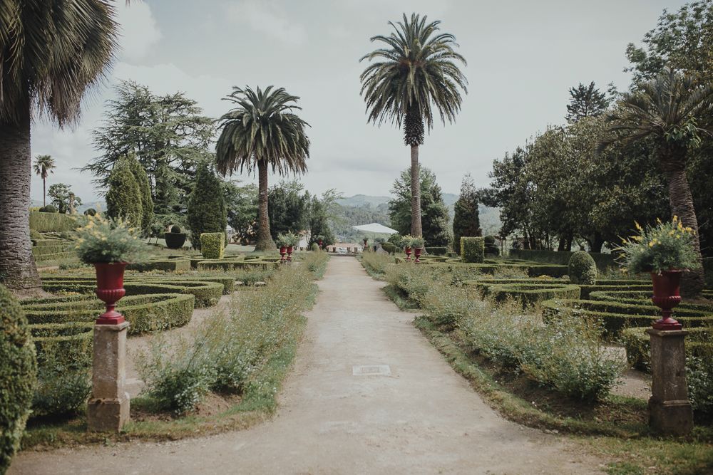 A palm tree-lined pathway through formal gardens with stone pillars.
