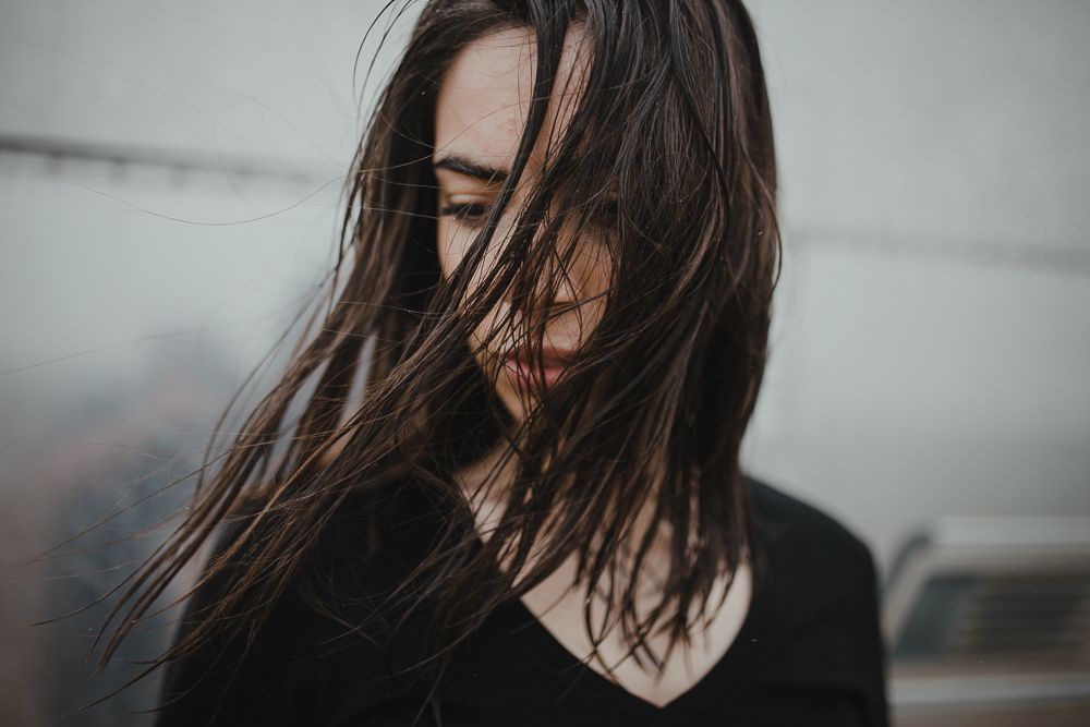 Dark moody portrait with windswept hair against a light background.