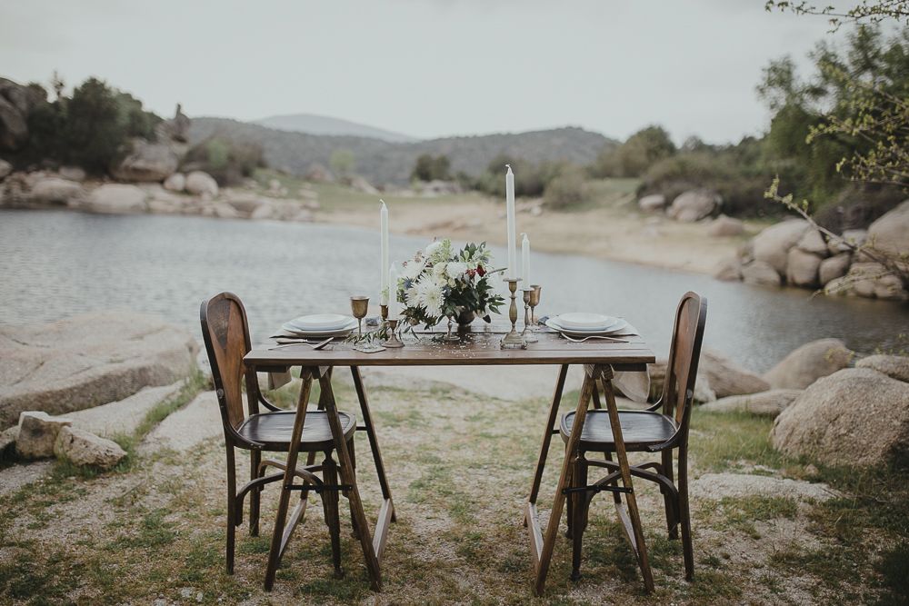 Intimate dining setup with two chairs at rustic table by a mountain lake.