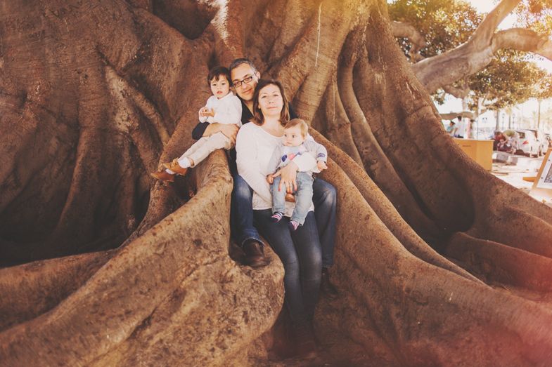 A family poses together among the massive exposed roots of an ancient tree.