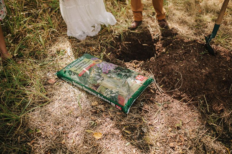 Green time capsule box being buried in dirt during outdoor ceremony.