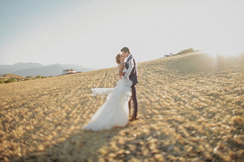 Newlyweds embrace in golden sunset light on rolling hills in Italian countryside.