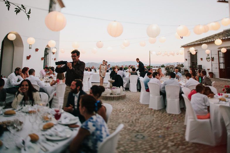 Evening wedding reception with guests seated at decorated tables under warm paper lanterns.