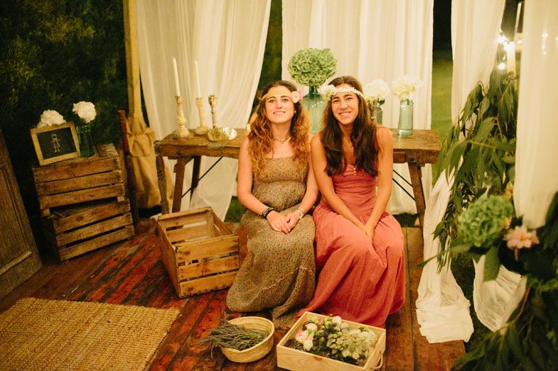 Two party guests in formal dresses seated on rustic wooden furniture at an event.