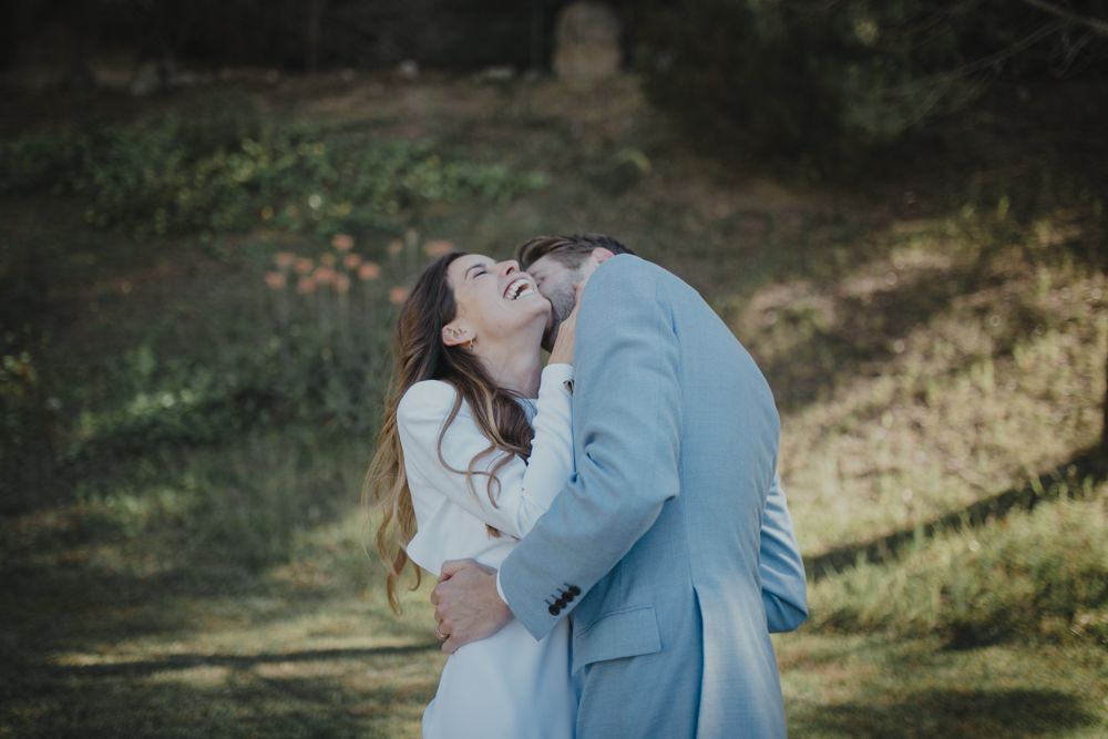 Intimate moment between couple in light blue suit and white wedding dress outdoors.