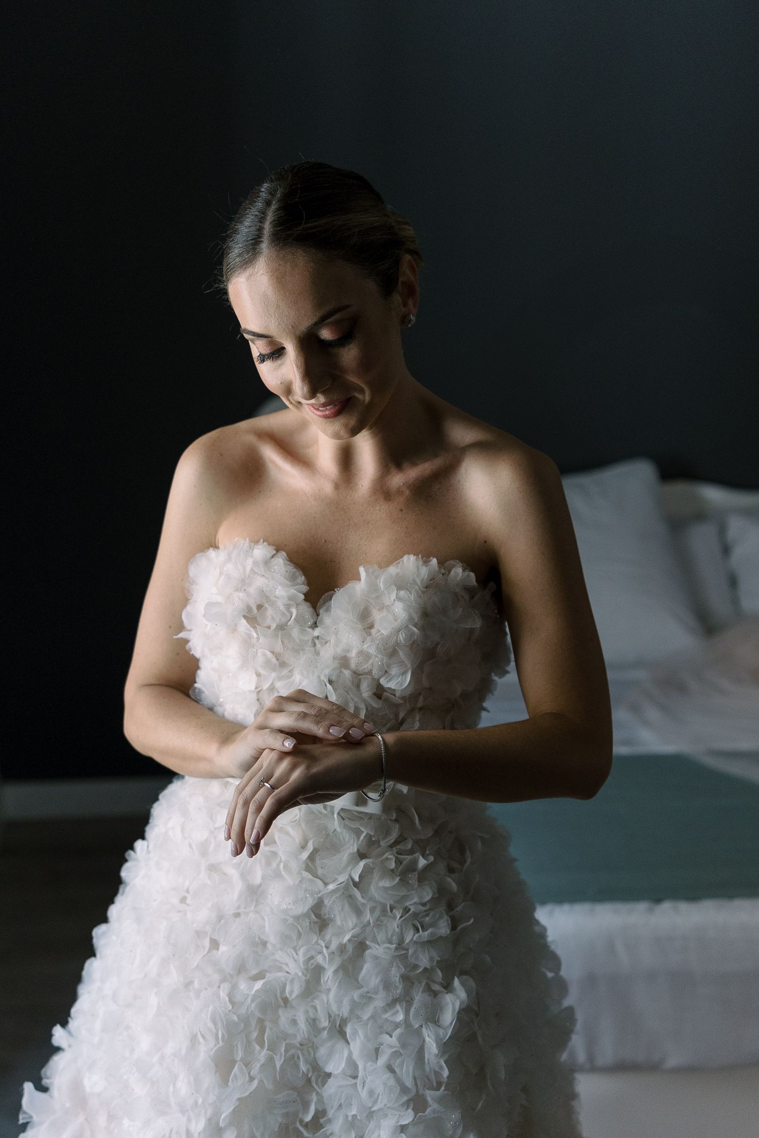 Bride in textured strapless wedding gown looking down in dramatic lighting.