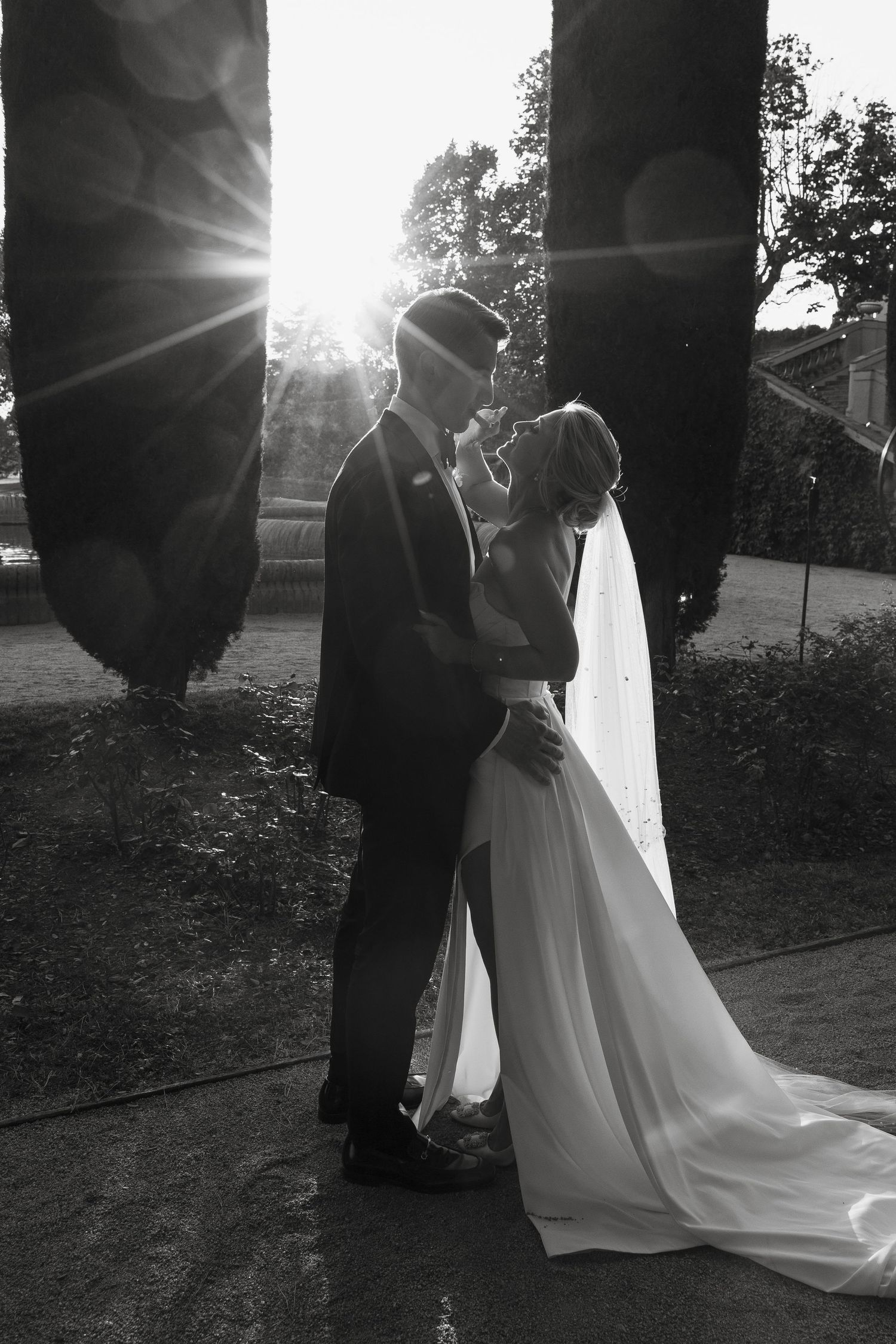 Romantic black and white silhouette of couple against sunlit garden pillars.