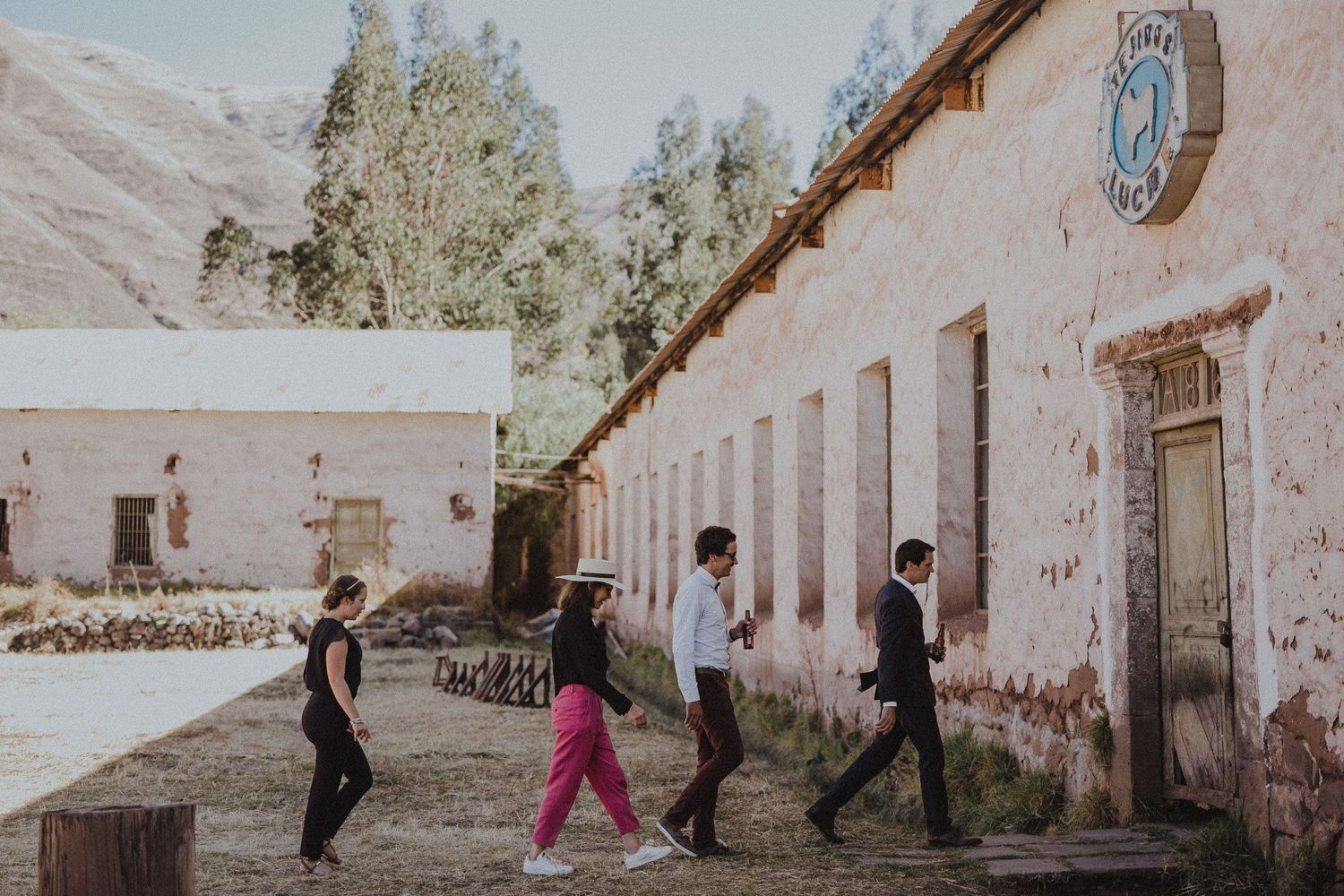 People walking along a rustic colonial building with mountains in the background.