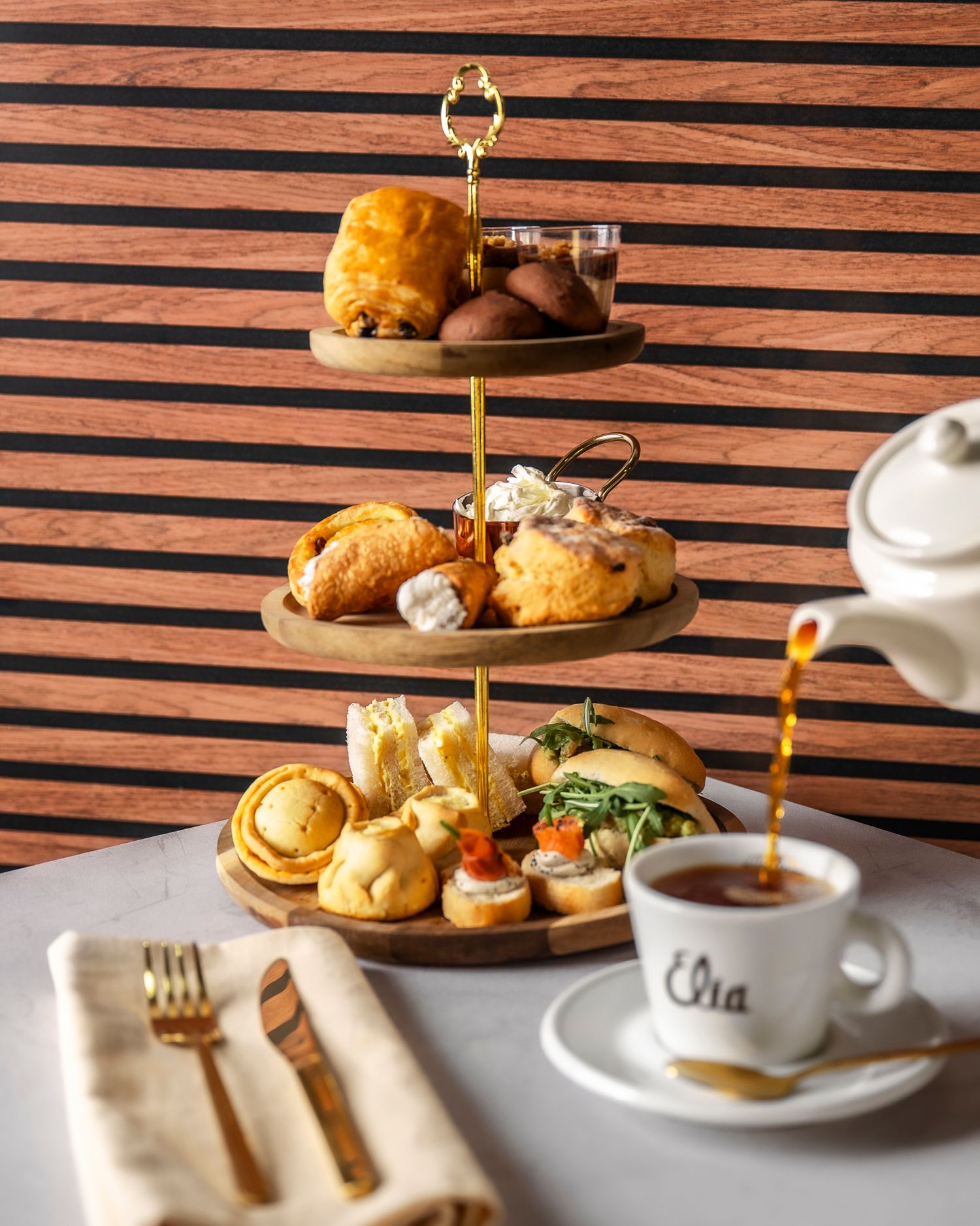 High tea service with mini sandwiches and pastries arranged on a tiered stand against wooden panels.