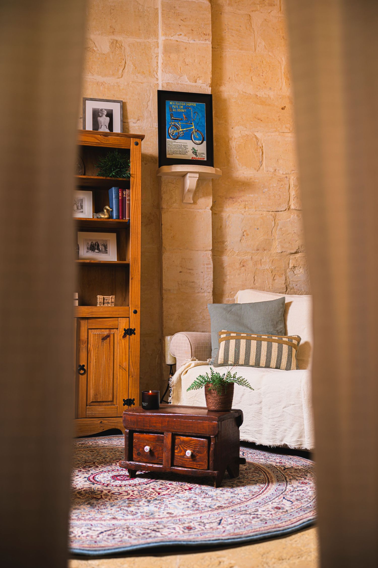Cozy rustic living room with stone walls, wooden bookcase, white sofa, patterned rug, and antique coffee table.