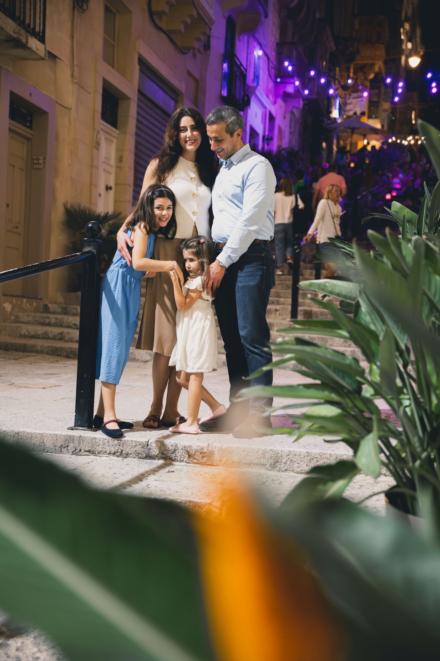 Family of four enjoying a festive night out on a charming Mediterranean street lit with purple lights.
