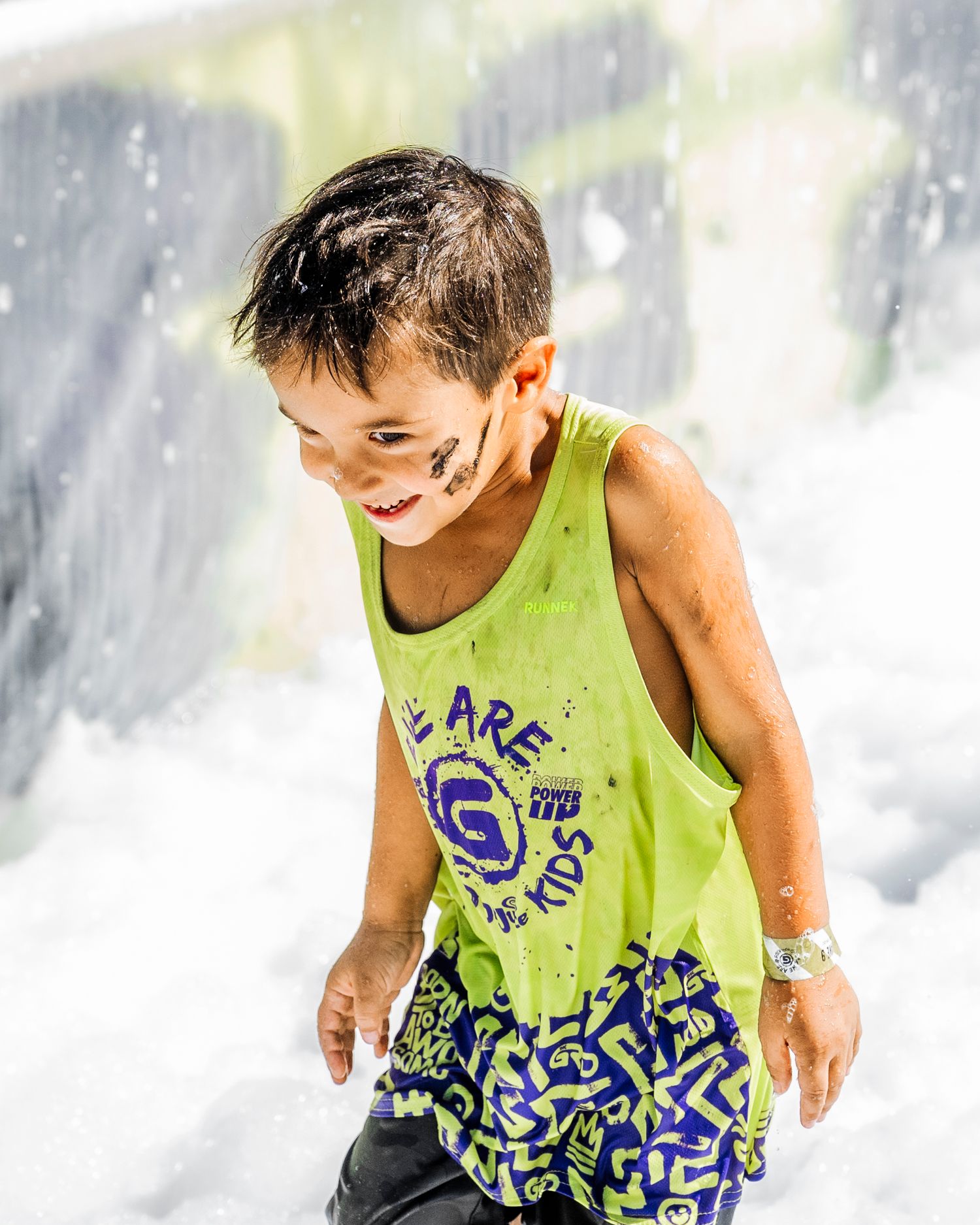 Kids splashing through water obstacles in bright yellow tank tops during outdoor event.