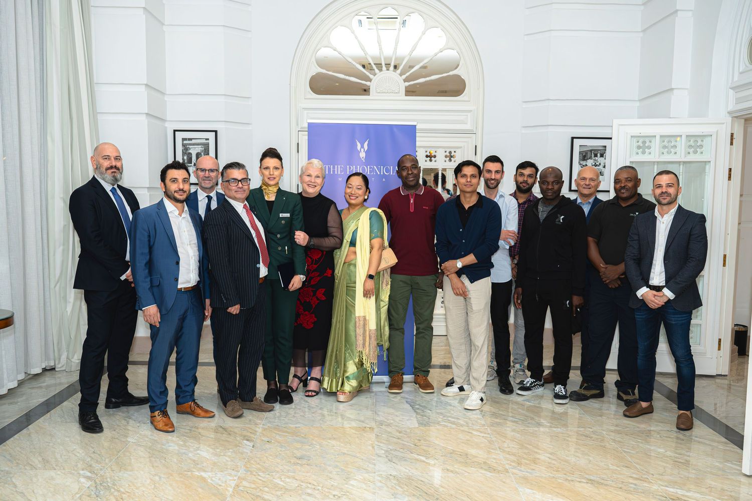 Large group photo of business professionals lined up against Phoenicia backdrop in marble hallway.