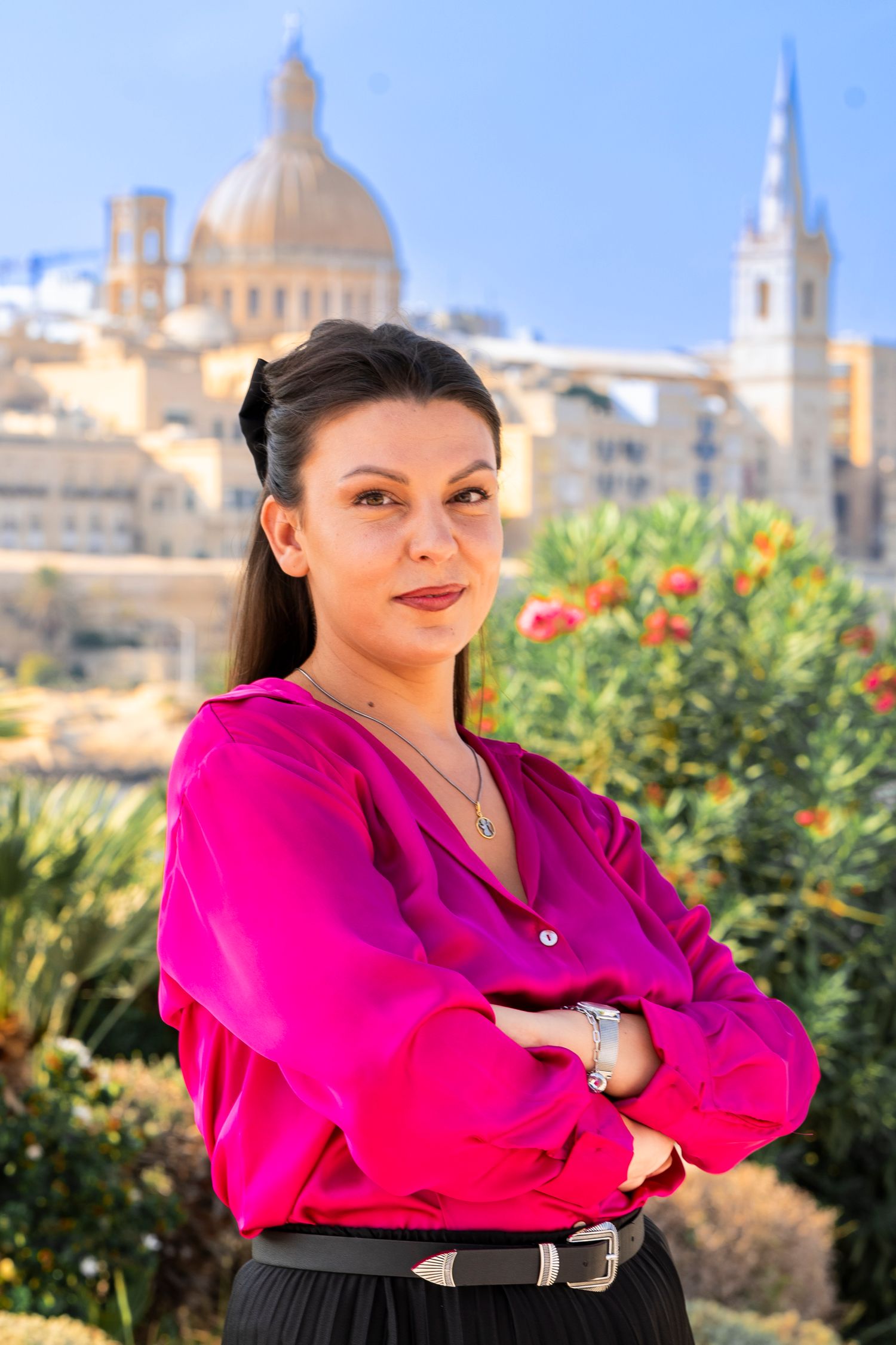 Person in bright pink shirt posing against Mediterranean cityscape with domed buildings.
