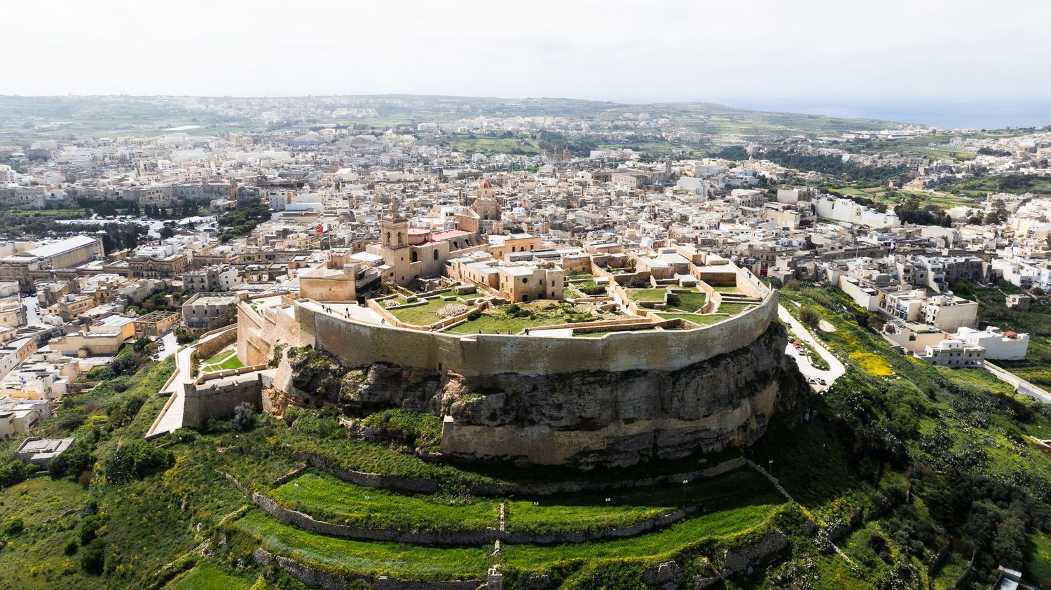 Panoramic aerial view of a sprawling Mediterranean city with white buildings and mountainous terrain.