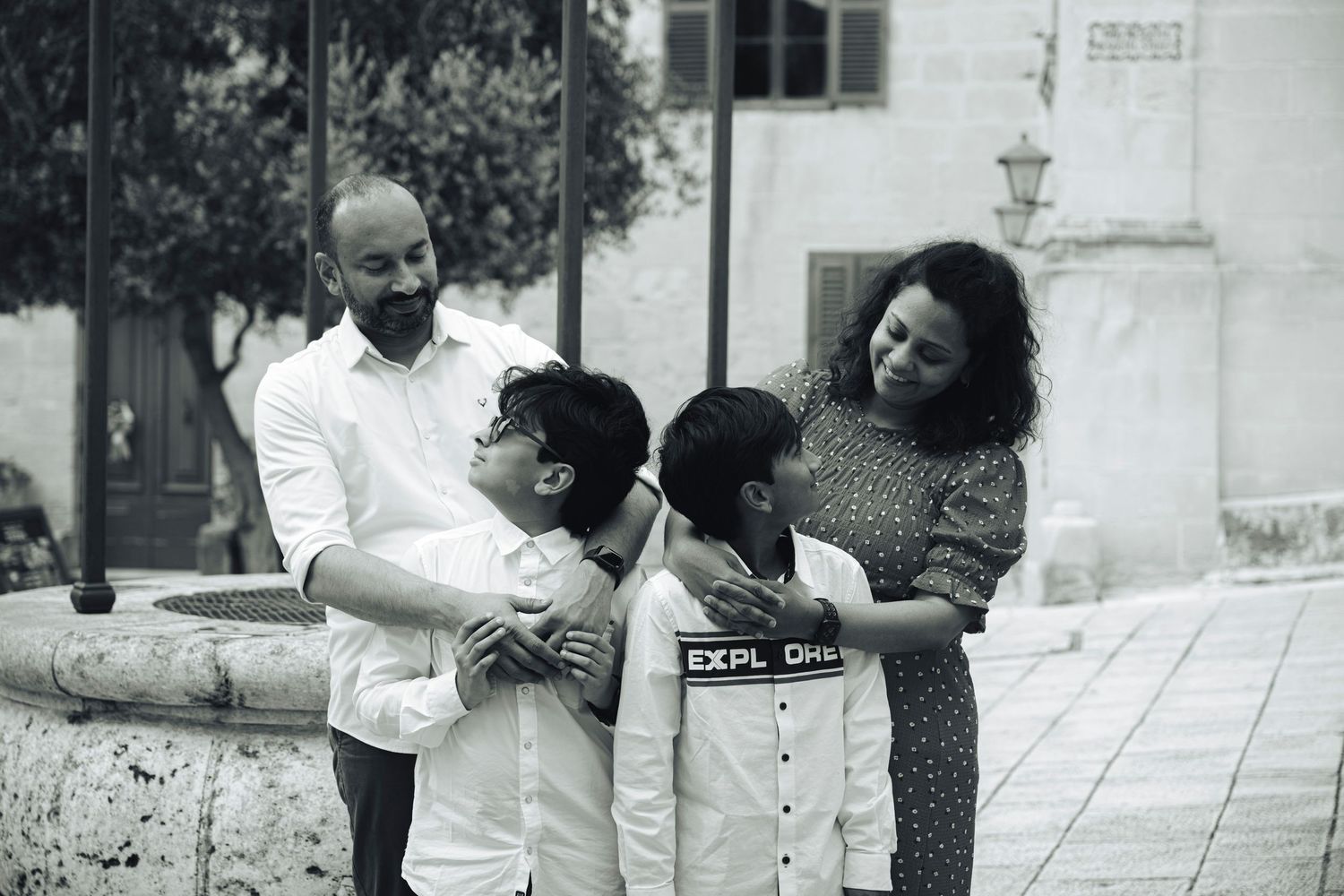 Black and white family portrait of parents with two young boys in a charming outdoor plaza setting.