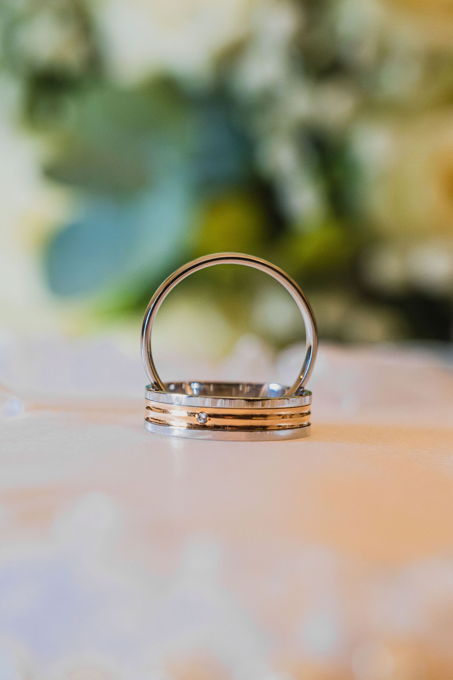 Close-up view of silver wedding rings arranged in a row on a blurred beige surface with soft bokeh background.