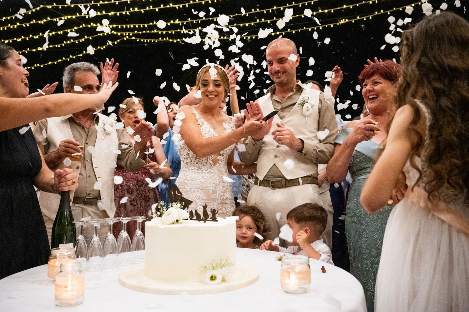 Joyful wedding celebration with guests throwing confetti near a tiered white cake.