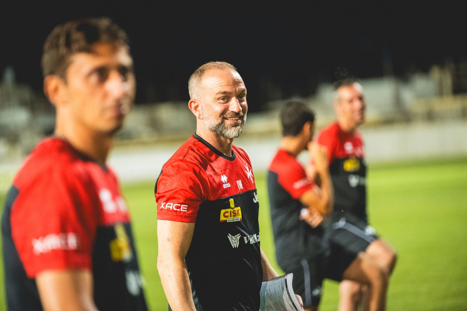 Soccer team in red jerseys gathered on field during evening training.