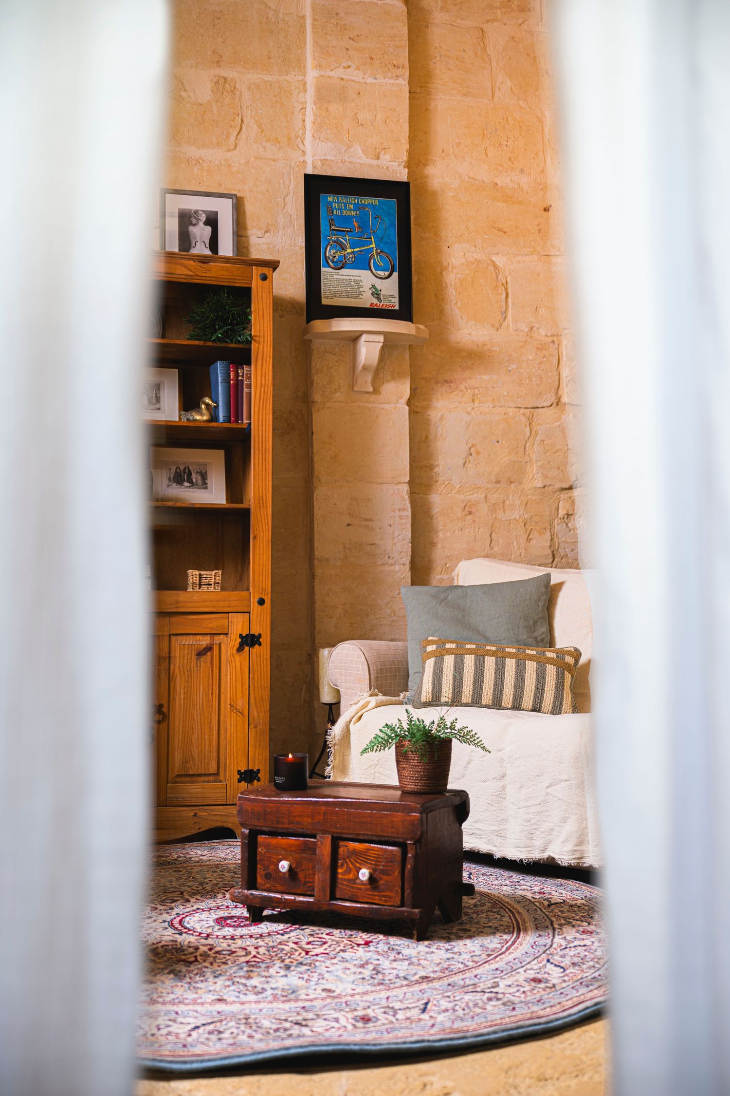Cozy reading nook with wooden cabinet, oriental rug and cushioned seating against stone walls.