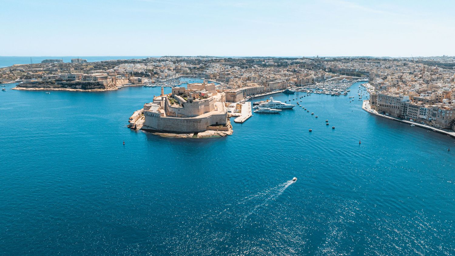 Panoramic aerial view of Malta's Grand Harbor with historic buildings and blue Mediterranean waters.