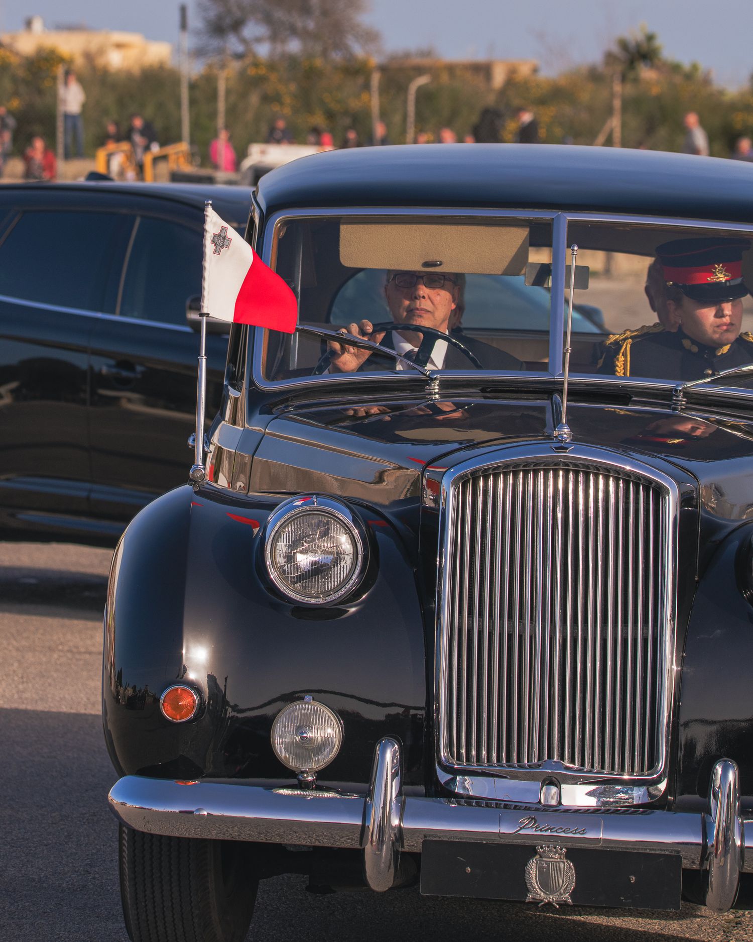 Classic vintage black luxury car with flag displayed during ceremonial procession.