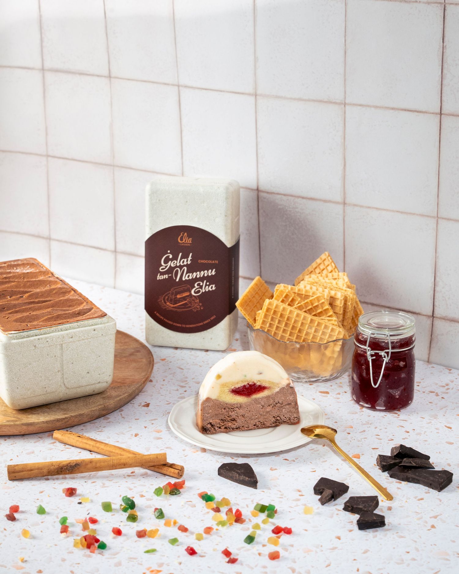 Chocolate dessert display with cake slices and wafers on white tiled background.