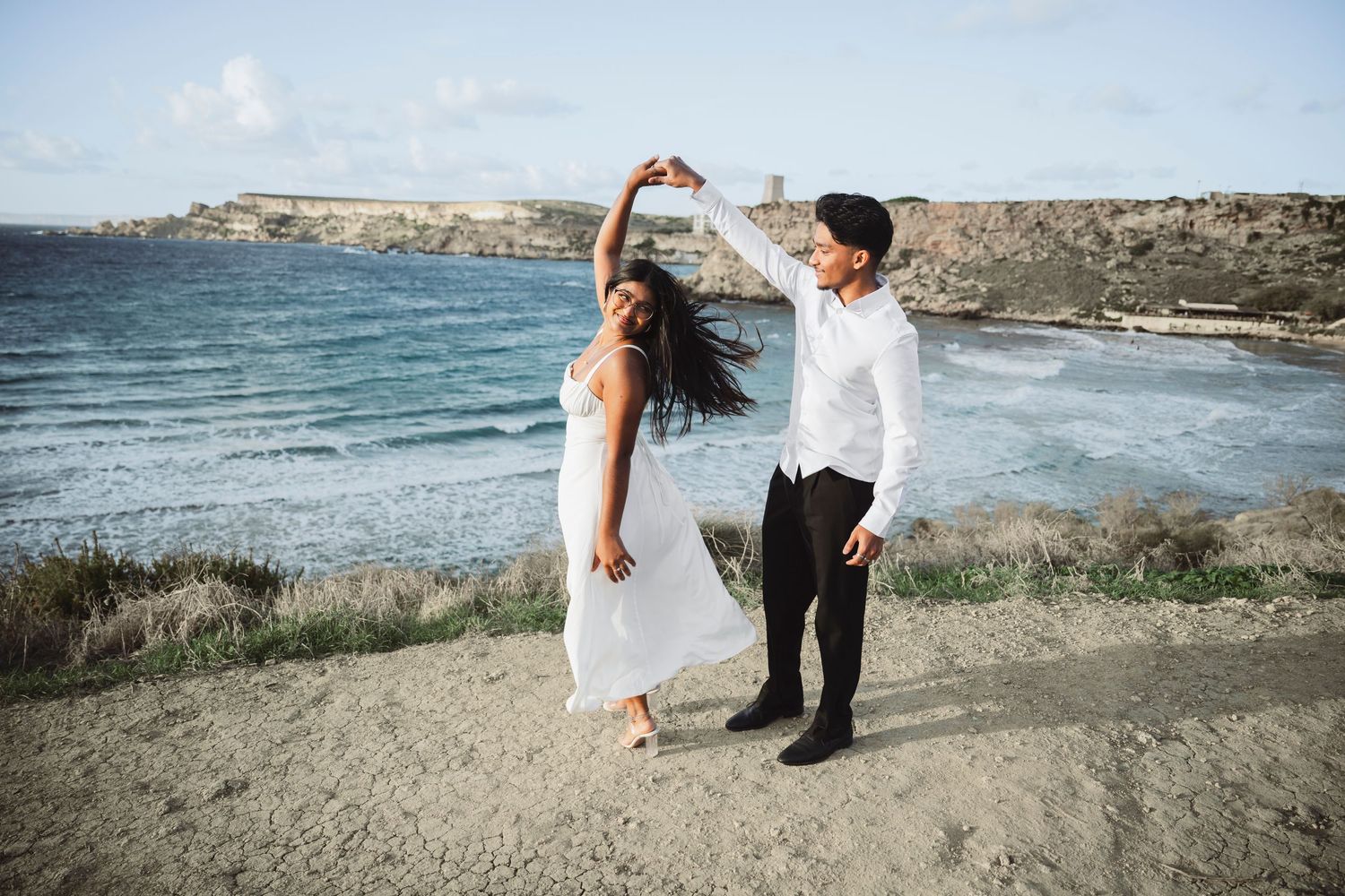 Couple posing for romantic photos along Mediterranean coastline with cliffs and ocean.