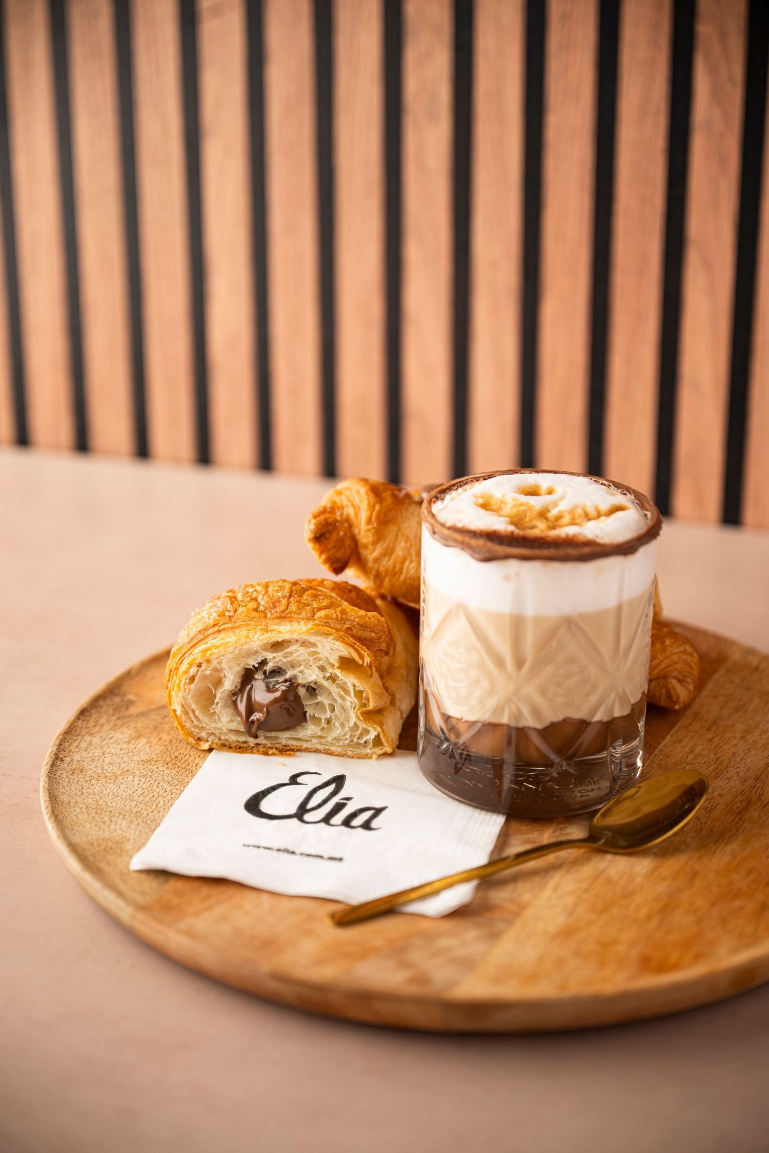 A series of wooden serving boards with coffee drinks and pastries arranged in a minimalist style against a striped background.