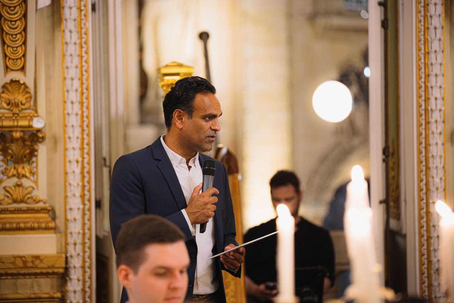 Elegant dinner event in gilded palace room with ornate gold details and chandeliers.