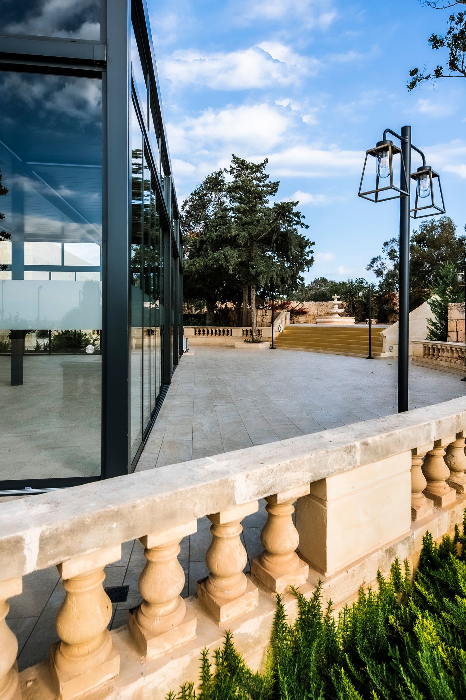 Modern rooftop terrace with glass railings and ornate stone balustrades against a blue sky.