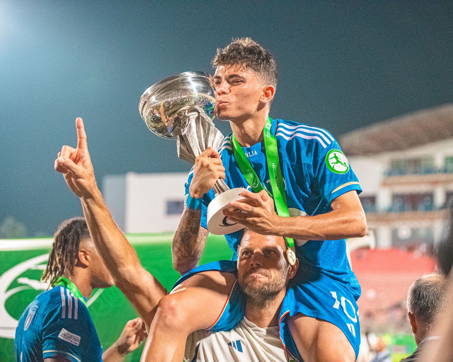 Soccer players in blue uniforms celebrating with a trophy after winning a championship match.