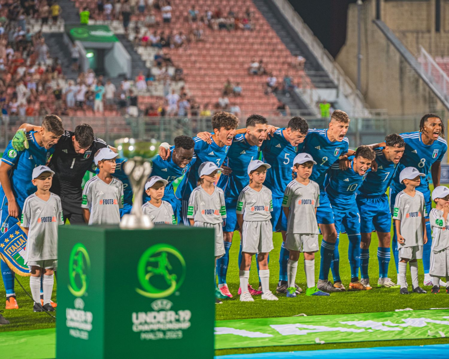 Soccer teams lined up on field before match with event signage visible.