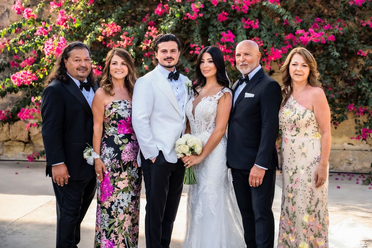 Wedding party members smiling and posing for formal photos with pink floral backdrop.