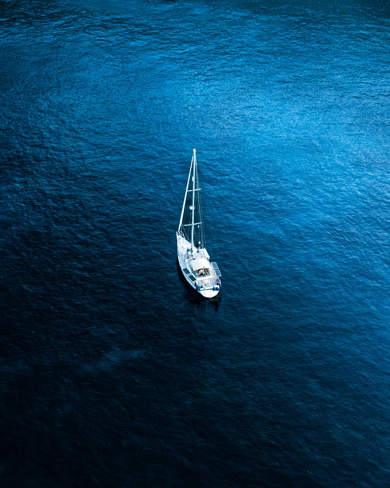 Series of sailing boats anchored in deep blue Mediterranean waters at dusk.