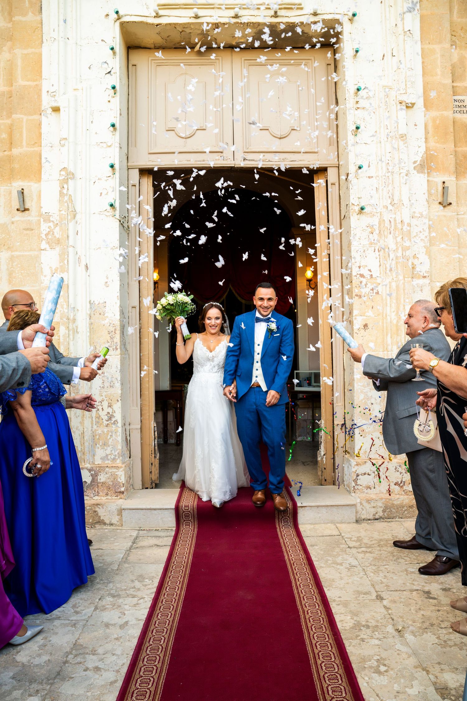 Wedding party exit with guests throwing confetti outside stone church entrance.