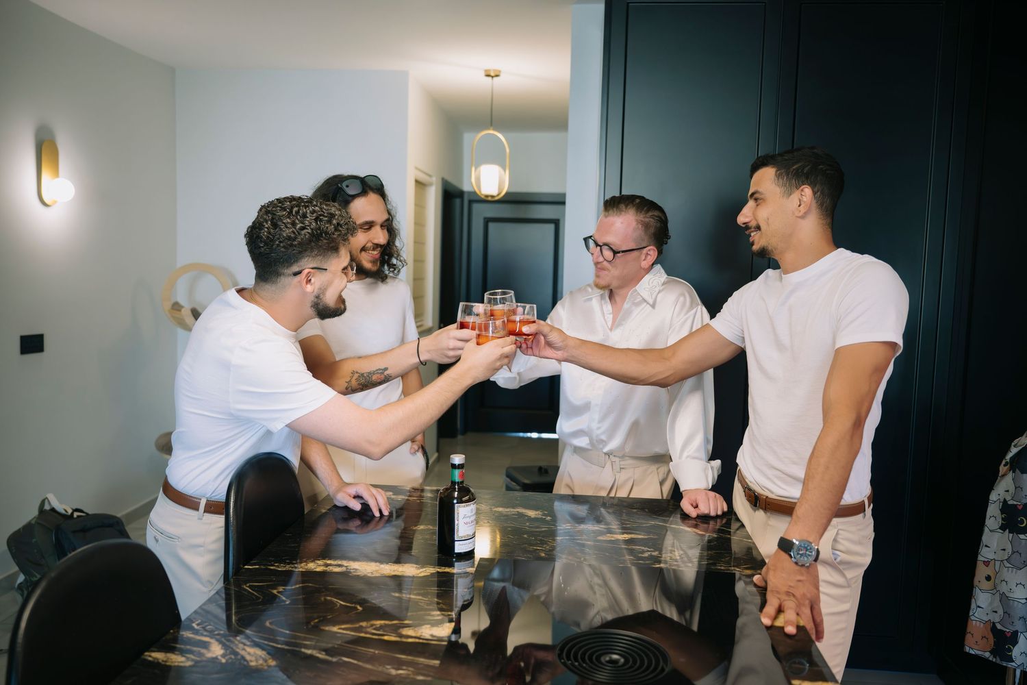 Four men toasting drinks around a glass table in a modern dining room during a celebration.