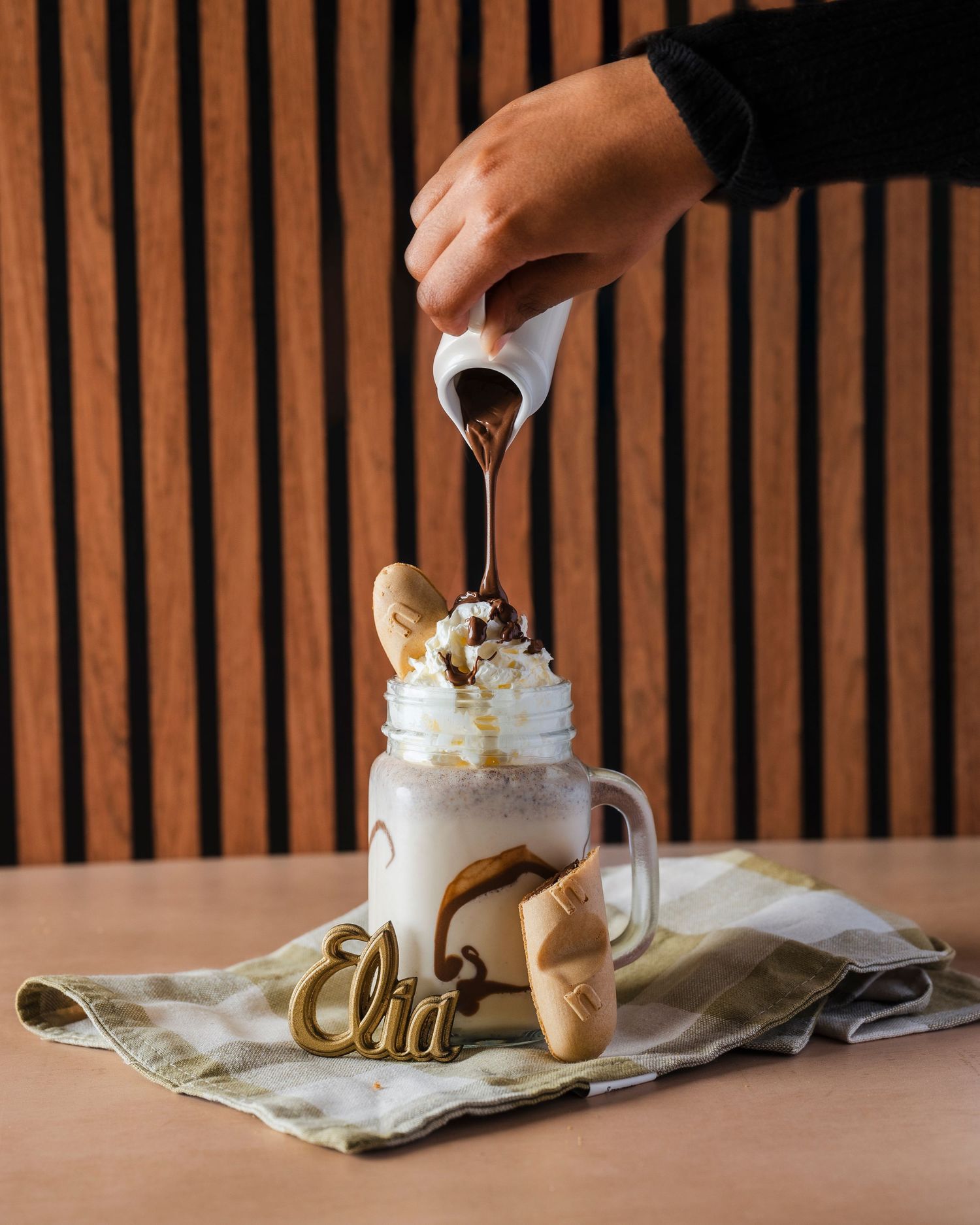 Pouring cream into a white mug topped with whipped cream and garnished with cookies.