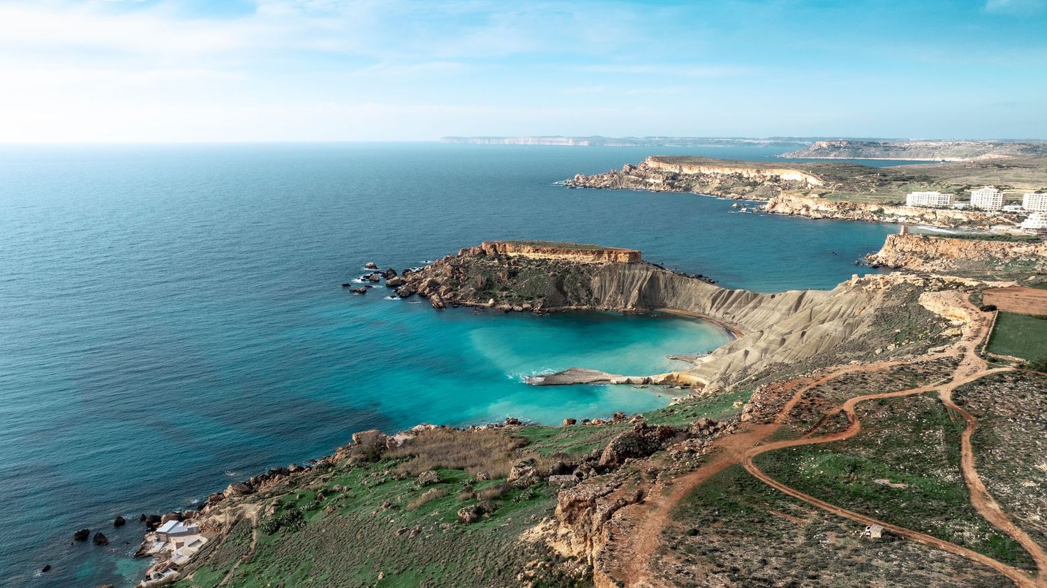 Panoramic coastal landscape showing turquoise waters and rocky cliffs against blue sky.